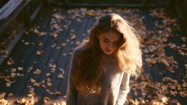 Autumn light bathes a young woman in warm tones on a leaf strewn wooden platform serene lifestyle portrait