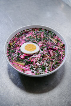 Vibrant chilled beet soup served in a white bowl with a halved boiled egg, fresh dill and chopped vegetables. A colorful Eastern European cold soup perfect for summer meals and traditional recipes.