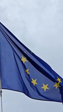 Close up view of the European Union flag with its circle of yellow stars on a blue background, waving slowly and majestically in the wind against a cloudy and overcast sky