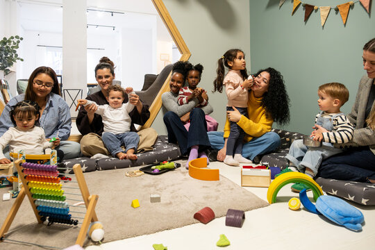 Diverse women and young children sitting on the floor playing with toys in a modern kindergarten
