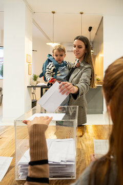 Woman holding baby depositing ballot into a transparent box during elections