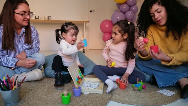 Two kindergarten teachers playing educational games with two little girls sitting on a carpeted floor