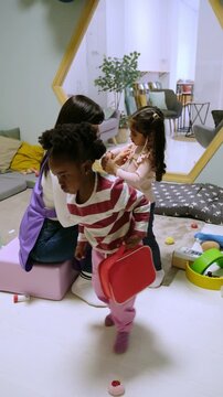 Diverse children playing with a toy medical kit and a teacher in a classroom