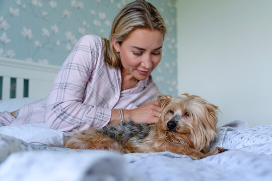 Woman spends time with her small dog on a bed in a cozy room with floral wallpaper during a quiet afternoon