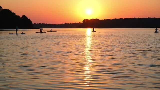 Moscow. Russia. 23.07.2026 People are paddle boarding on a lake at sunset. Silhouette of man and woman riding sup boards on water during golden hour. Outdoor sport and nature recreation.