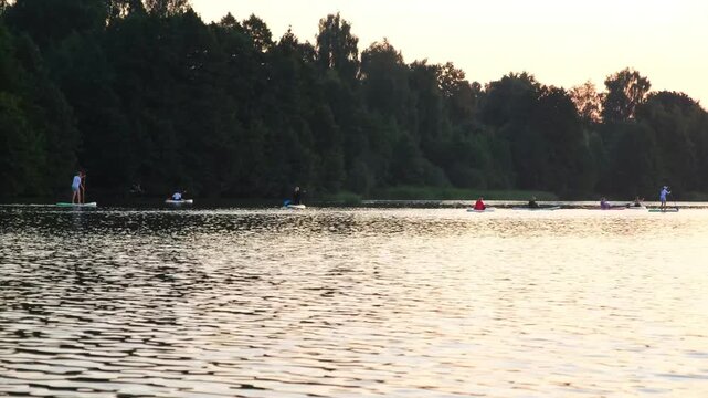 Moscow. Russia. 23.07.2026 People paddle boarding on a calm lake during a golden sunset. Man and woman enjoying outdoor water sport activity. Scenic summer evening recreational lake travel.