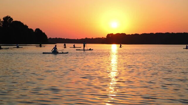 Moscow. Russia. 23.07.2026 People stand on paddle boards on lake during sunset. Men and women enjoy water sport in summer evening. Active lifestyle, recreation and vacation at riverside.