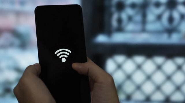 Close-up of hands holding a mobile phone showing a Wi-Fi error symbol against a rainy window background. Concept of bad internet connection and signal problems