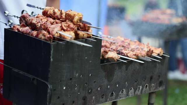 Man grilling meat skewers on a metal brazier outdoors. Cooking process of traditional shashlik barbecue at a picnic event. Delicious food preparation concept.