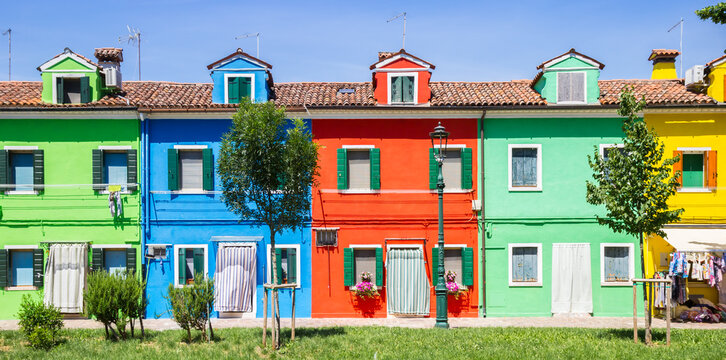 Panorama of symmetrical colorful houses behind young green trees in Burano, Venice, Italy