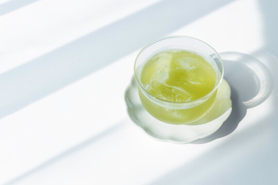 Glass of iced green tea in sunlight on white background with copy space
