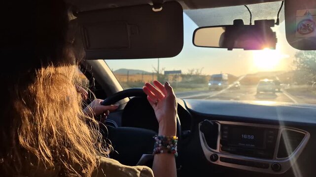 Woman driving car along a coastal highway while enjoying the sunset view. Static interior point of view shot.