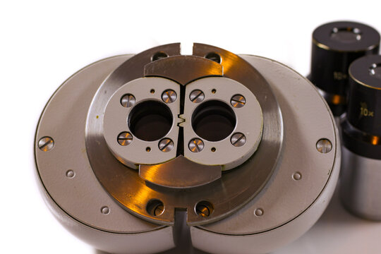 Macro close-up of a stereo microscope objective mount and optical head with precision metal components isolated on a white background.