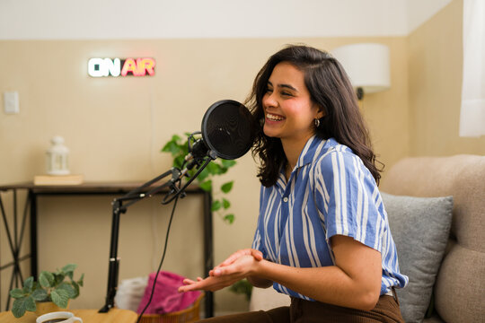 Female podcaster recording audio content from home studio, speaking into microphone with on air sign glowing