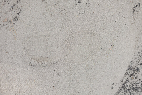 Single boot footprint imprint in grey sand texture close up