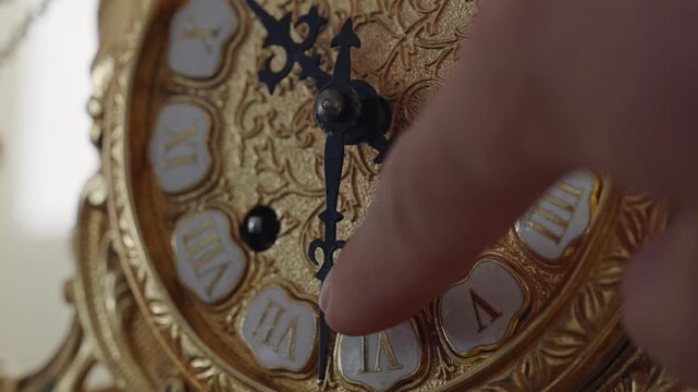 Human finger setting the time on a vintage golden clock