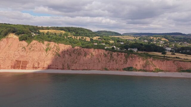 Aerial drone footage of the striking red sandstone cliffs at Jacob's Ladder Beach in Sidmouth, East Devon, England. The video captures the Jurassic Coast, dramatic coastal scenery, and the English Cha