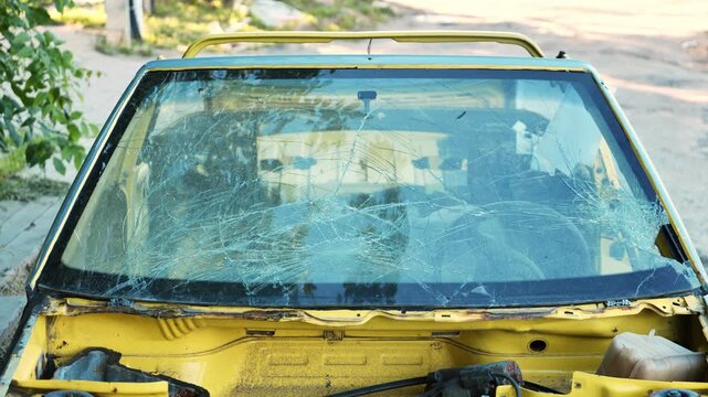 Broken windshield on abandoned yellow car showing severe damage from an accident