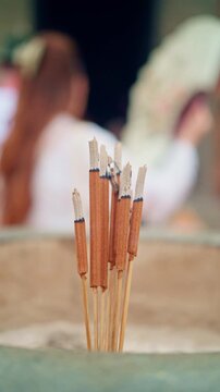Burning incense sticks with smoldering ash and thin smoke in soft diffused light, arranged in calm upright cluster with warm neutral tones and quiet meditative mood