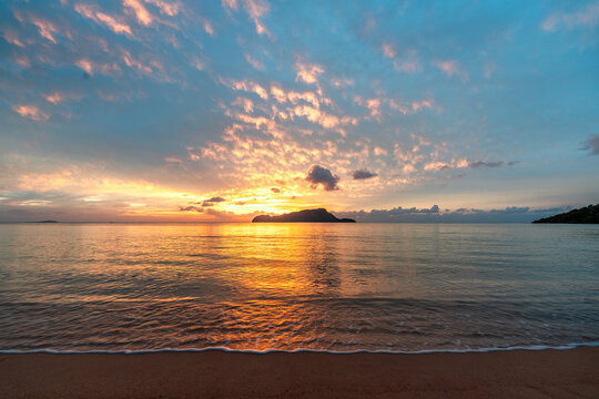 Beautiful sunset over the ocean with orange colour clouds and view on small island