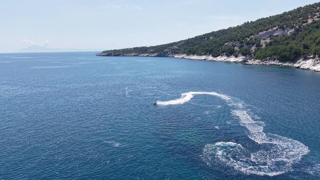 A long white wake gradually straightens across open water beside a distant natural coastline.