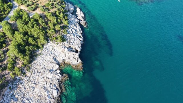 High-angle drone view gradually reveals a narrow coastal passage bordered by rugged rocks, green trees and clear blue seawater.