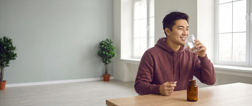 Young man taking a vitamin supplement with water at home. Autumn wellness, immune support, cold and flu prevention concept with copy space.