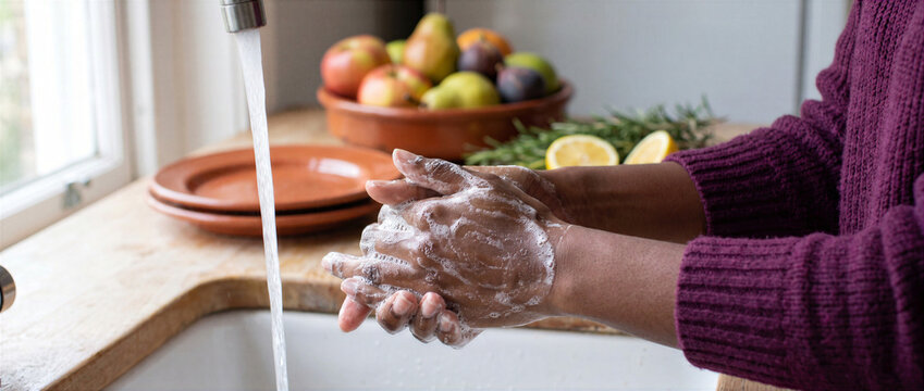 Person washing hands with soap under running water in the kitchen. Hygiene, infection control, autumn cold and flu prevention concept.