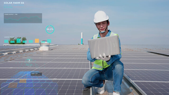 Asian male solar panel engineer in hard hat using laptop on factory roof with digital smart HUD overlay analyzing real-time photovoltaic energy output and system performance data