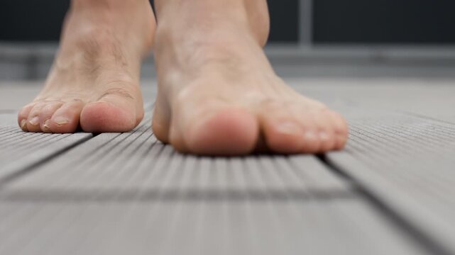 Close up of bare feet walking across composite terrace boards outside a modern house. Man stepping barefoot on balcony deck