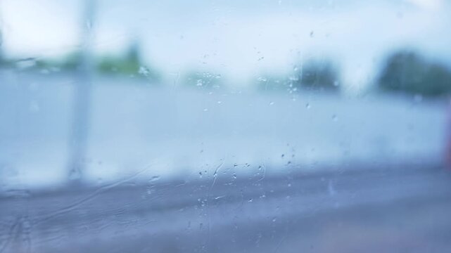 Raindrops on window blurring train view, traveling in wet weather
