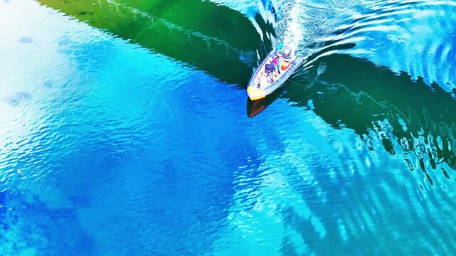 Small fishing boat with anglers passing beneath a bridge, creating reflections and rippling water as it leaves Irvine Harbour, Ayrshire, Scotland, aerial