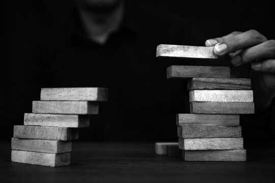 Hand placing wooden block tower stack in pyramid stair step with caution to prevent collapse or crash concepts of financial risk management and strategic planning and business challenge plan.