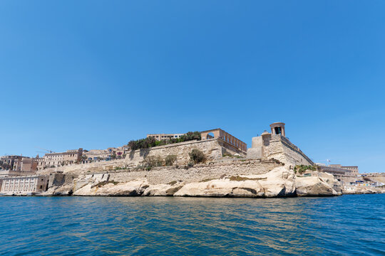 Historic limestone bastions and memorial cupola viewed from the sunny sea at Siege Bell War Memorial, Valletta, Malta
