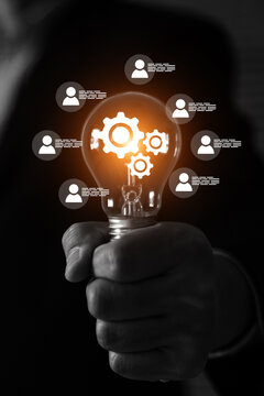 Businessman's hand with HR human resources icons on light bulb for leader or group teamwork people officer or business planning or team player and personnel management job performance.