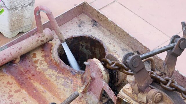 Powerful close-up of a heavily rusty anchor chain being actively pulled up and cleaned by a high-pressure water spray system.