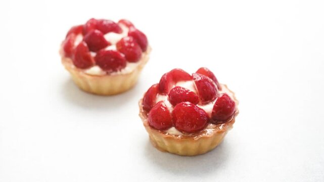 Two strawberry tarts with cream on white background
