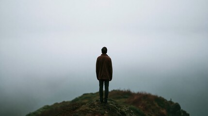 Obraz premium Man standing on a cliff edge looking out into the foggy distance