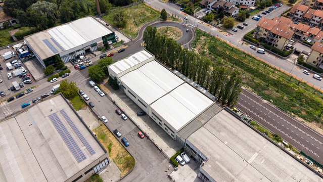 Aerial View of Industrial Zone: An expansive aerial perspective captures a modern industrial zone, featuring large factory buildings, warehouses, solar panels, and a busy road with vehicles.