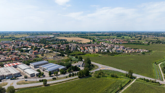 Aerial View of Rural Town and Industrial Zone: A sprawling rural town nestled amidst green fields, with an industrial zone featuring warehouses and solar panels in the foreground. Tavazzano con Villav