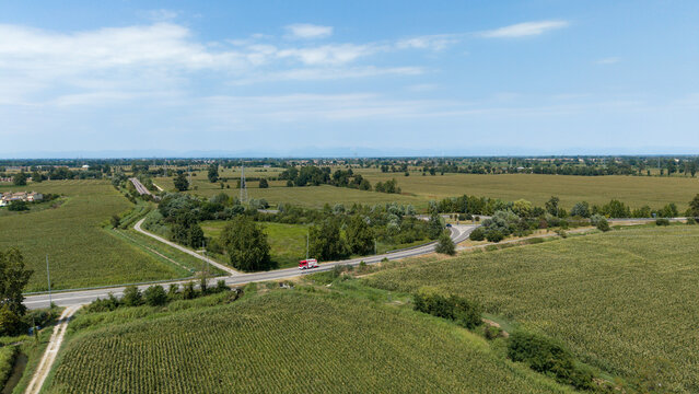 Rural Intersection in Green Fields: An aerial view captures a crossroads connecting vast expanses of lush green agricultural fields under a clear blue sky. Tavazzano con Villavesco, Lodi, Italy