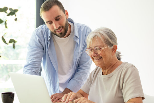 Young man assisting senior woman with a laptop, sharing knowledge and bridging the digital divide, highlighting patience, learning, and connection between generations