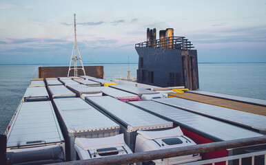 Top view of a ferry fully loaded with cargo trucks at sunset on the sea.