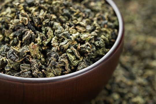 Dark wood bowl overflowing with Tie Guan Yin on full tea background