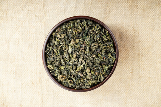 Overhead macro of green oolong in wooden cup on light burlap