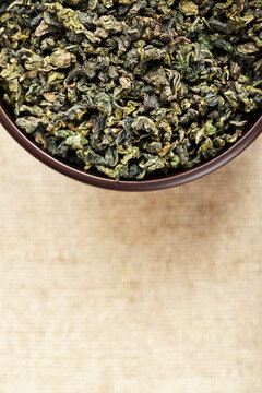 Top view closeup dark wood cup full of loose tea on natural fabric
