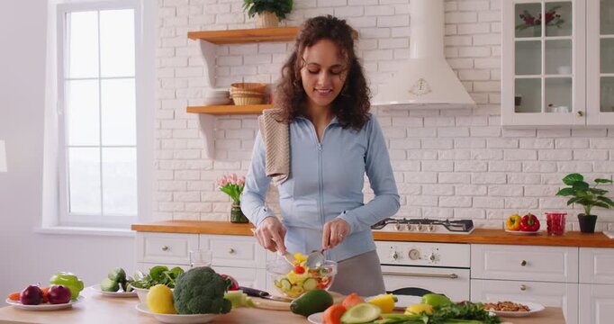 Happy fit dancing woman standing in modern kitchen cooking fresh vegetables mixing tasty salad in bowl, happiness and health, cooking and healthy eating, lively and cheerful atmosphere at home