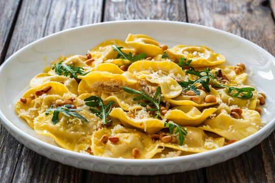 Cooked ravioli with pine nuts, rocket leaves and grated parmesan cheese on wooden table
