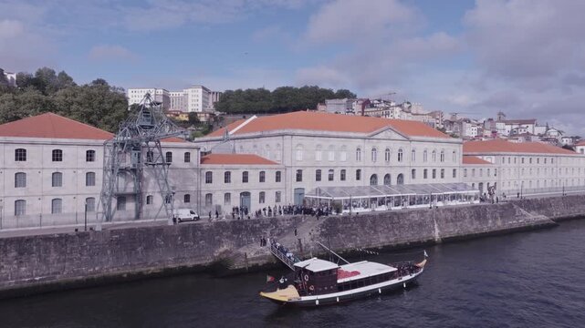 Aerial views of river Douro and a river boat docking to load passengers at a large old building. Porto, Portugal