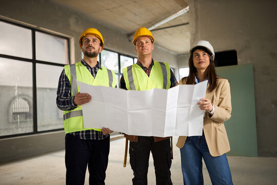 Female building contractor and her manual workers analysing blueprints at construction site.